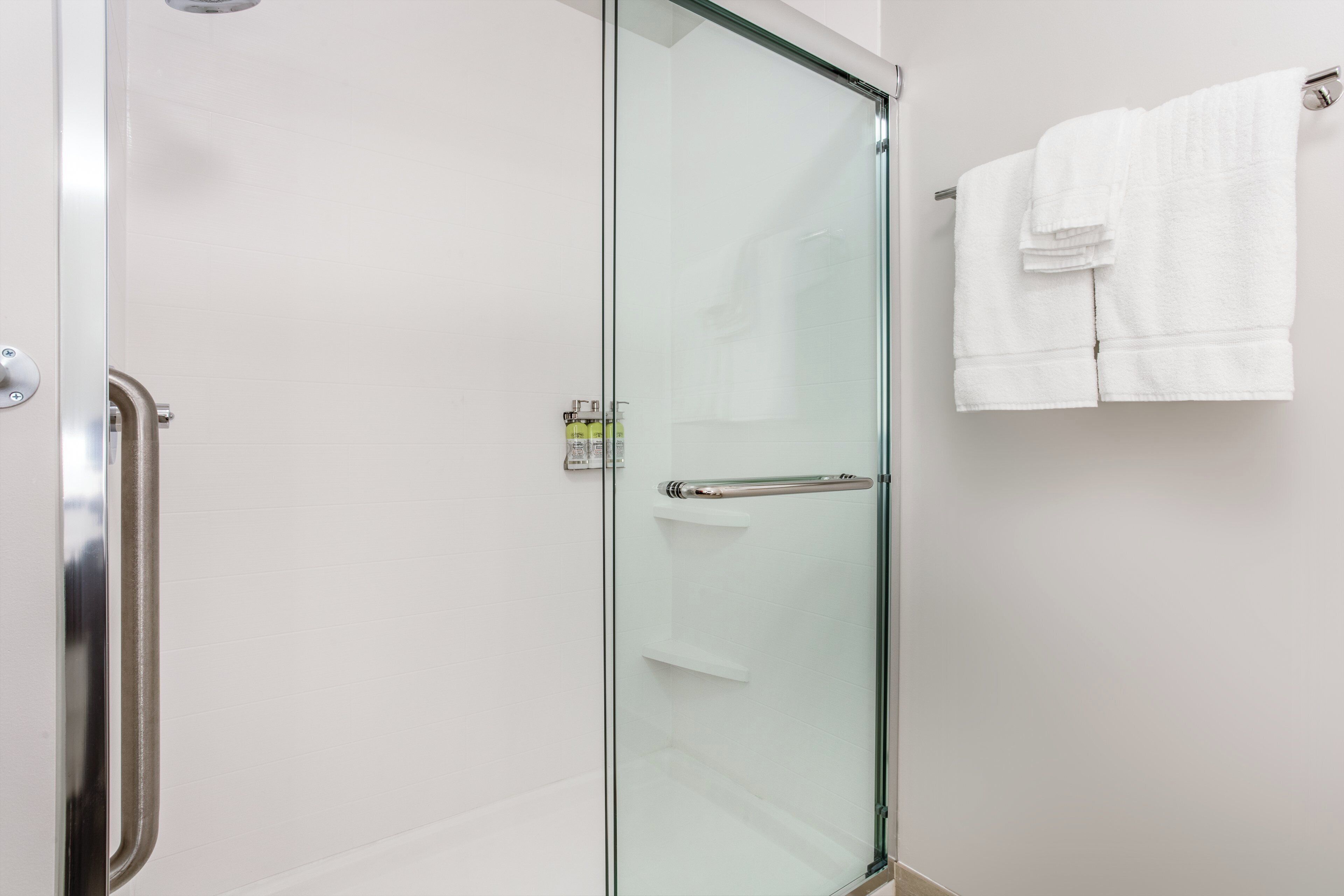 A glass-enclosed shower with a stainless steel handle and a towel rack with folded towels.