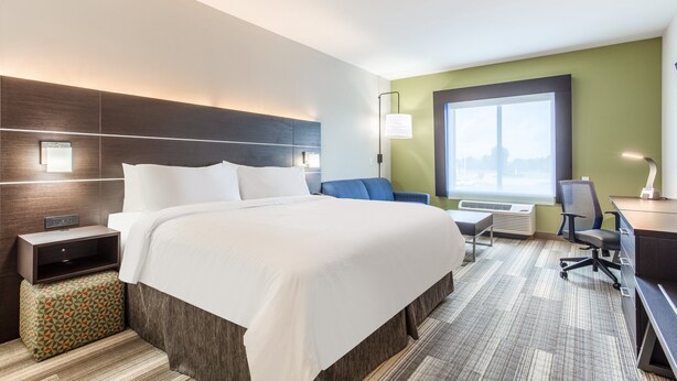 A hotel room with a large bed, a desk with a chair, a small table, a lamp, and a window with a view.