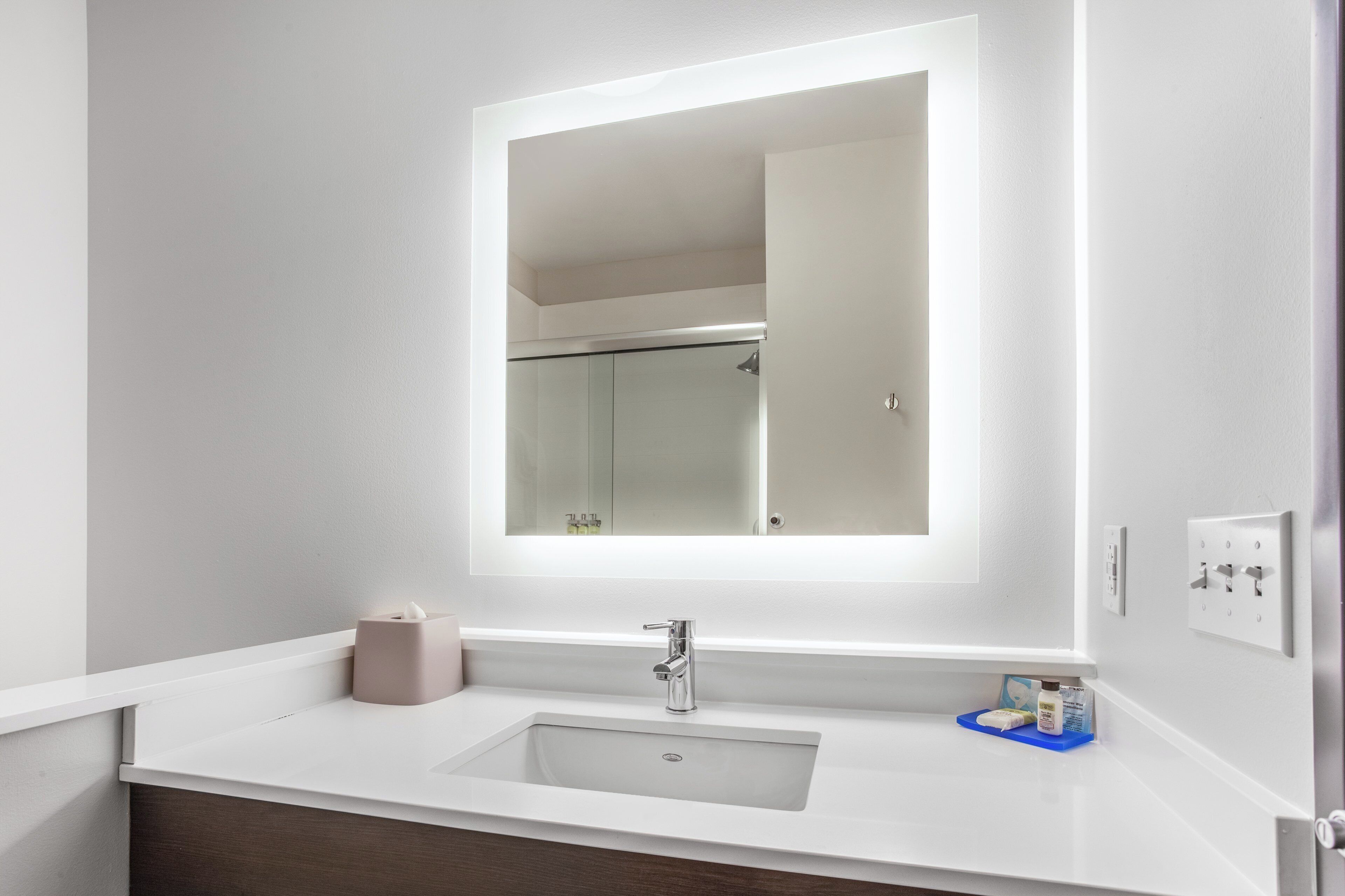 A bathroom with a white sink, a mirror, and a towel dispenser.