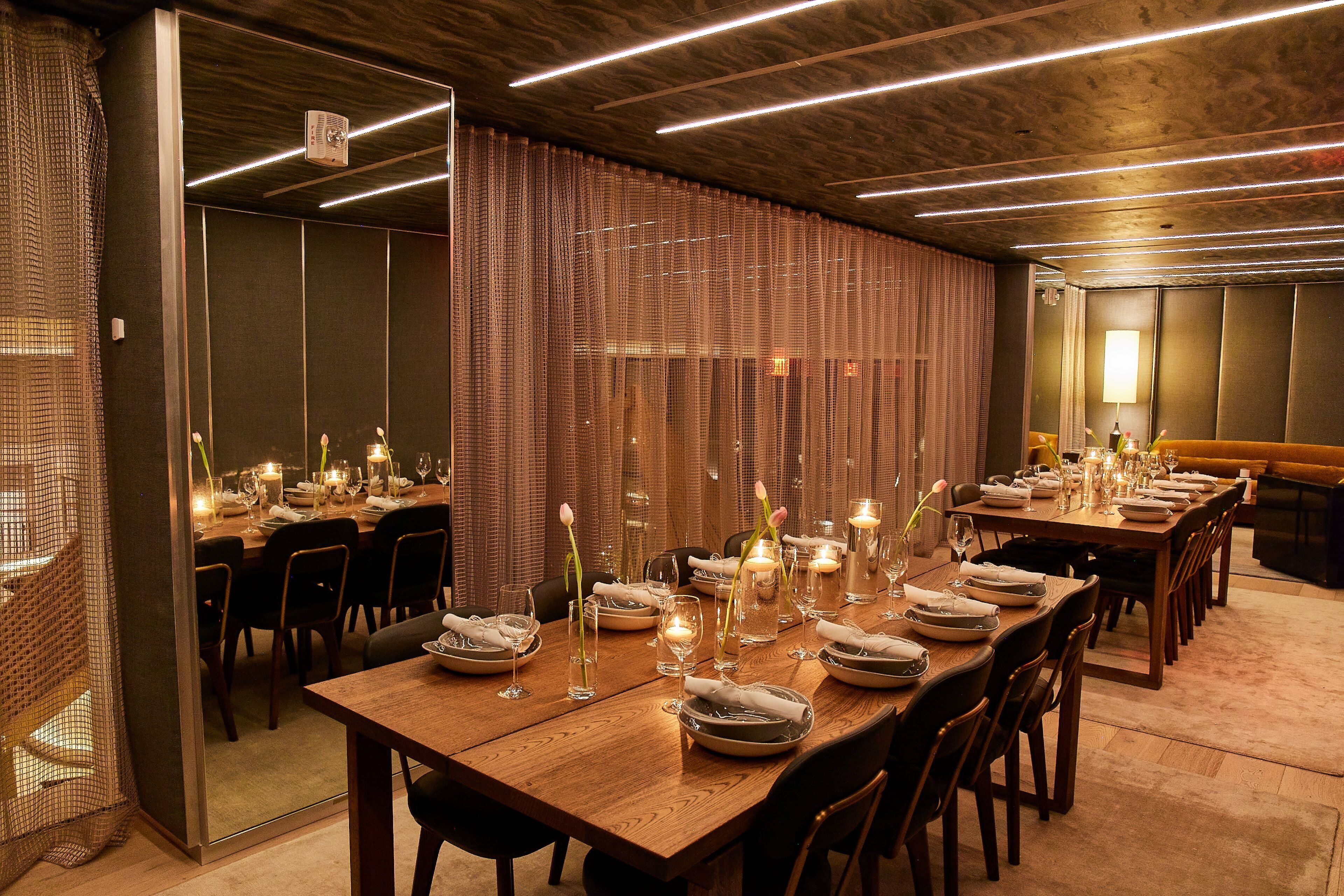 A dining area with long wooden tables set for a meal, featuring candles and floral centerpieces.