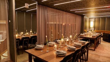 A dining area with long wooden tables set for a meal, featuring candles and floral centerpieces.