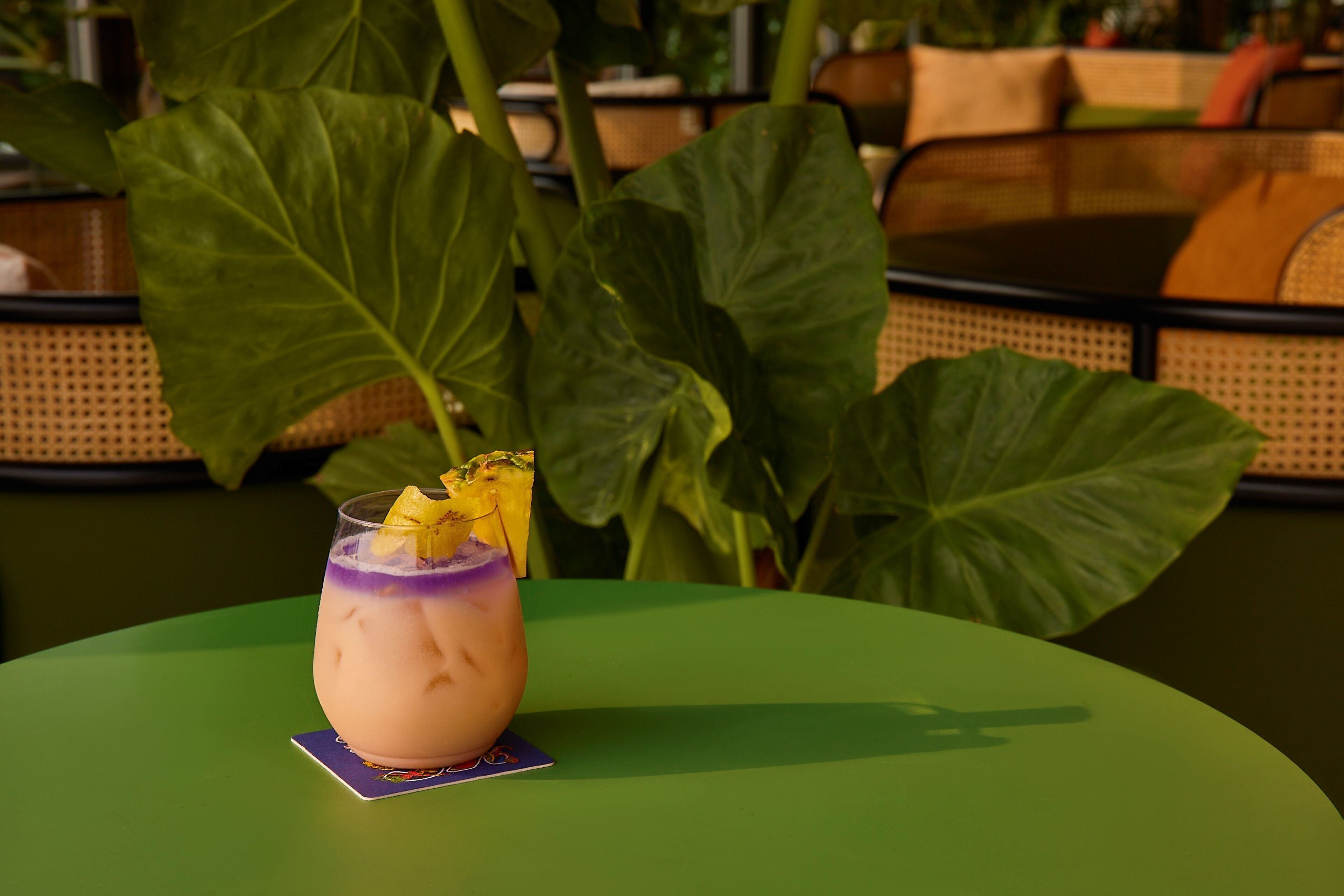 A cocktail on a green table with large green leaves in the background.