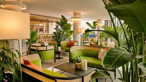 A modern lounge area with green seating, a bar in the background, and abundant indoor plants. - Hotel Indigo Williamsburg - Brooklyn by IHG (Brooklyn)
