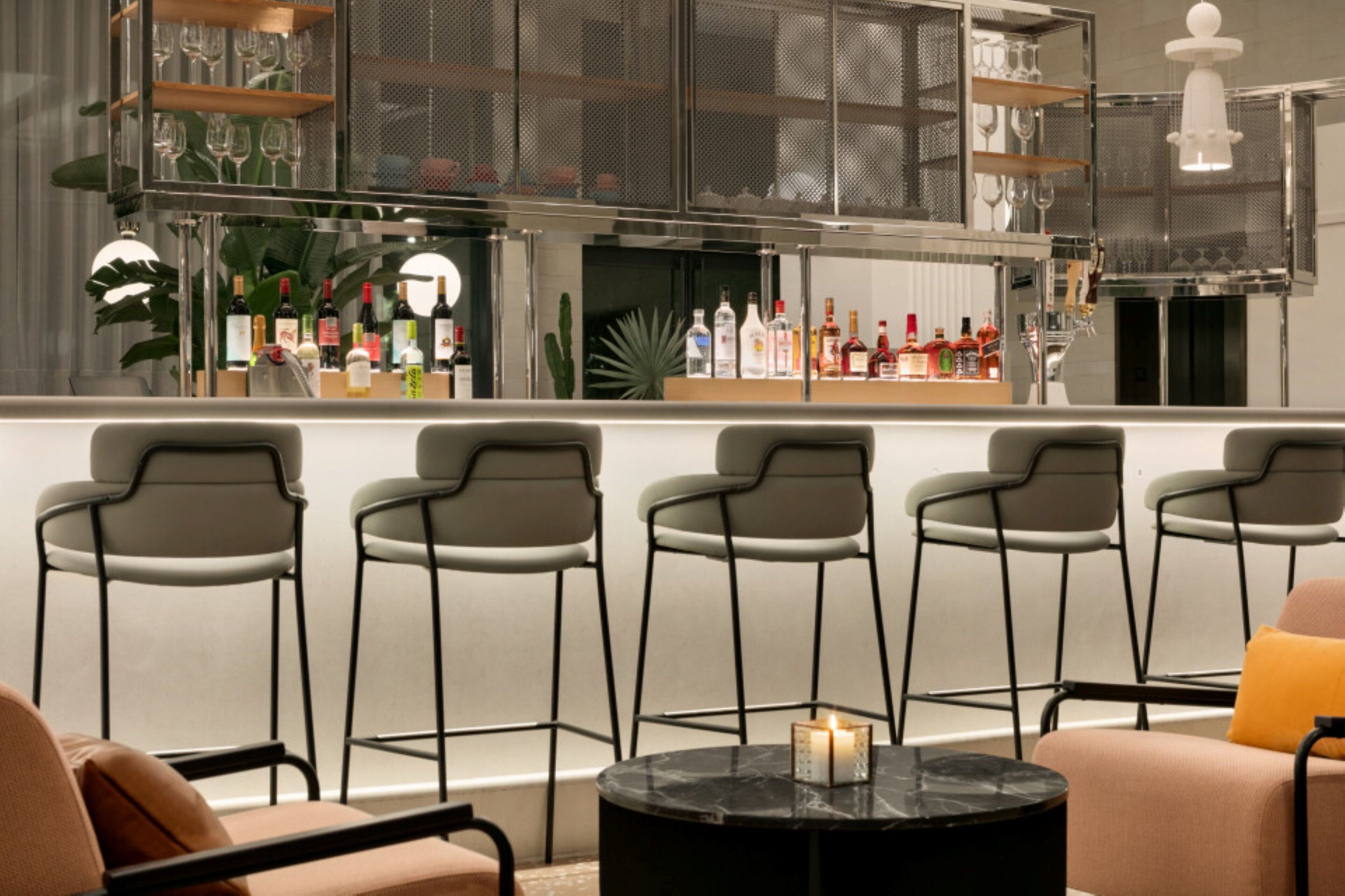 Een bar met een toonbank vol flessen, een zithoek met stoelen en een tafel met een kaars.