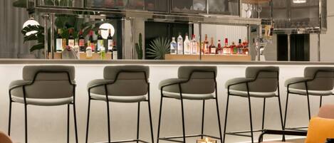 Een bar met een toonbank vol flessen, een zithoek met stoelen en een tafel met een kaars.