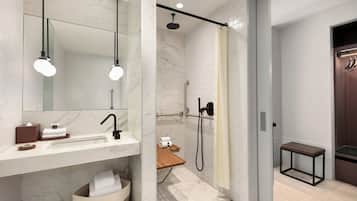 Een moderne badkamer met een marmeren wastafel, een douche met handdouche en een bankje.