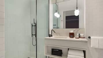 Een moderne badkamer met een douchecabine van glas, een witte wastafel met een marmeren blad en een spiegel boven de wastafel.
