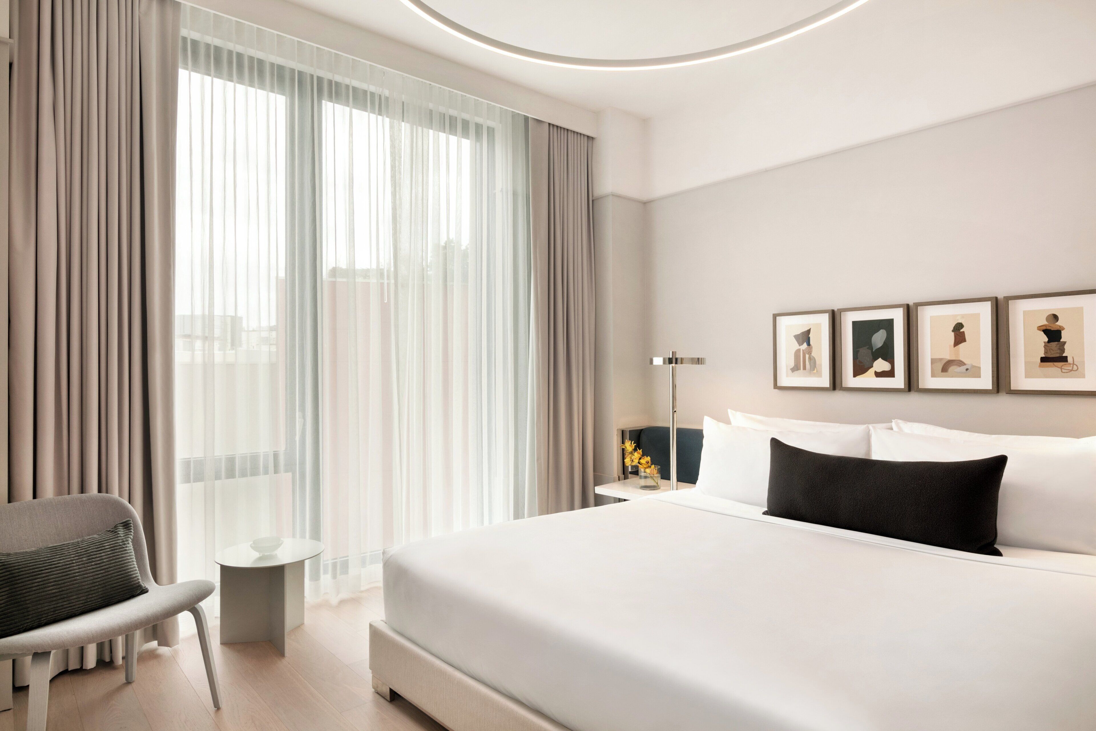 A hotel room with a bed, a chair, a bedside table, a lamp, and artwork on the wall.