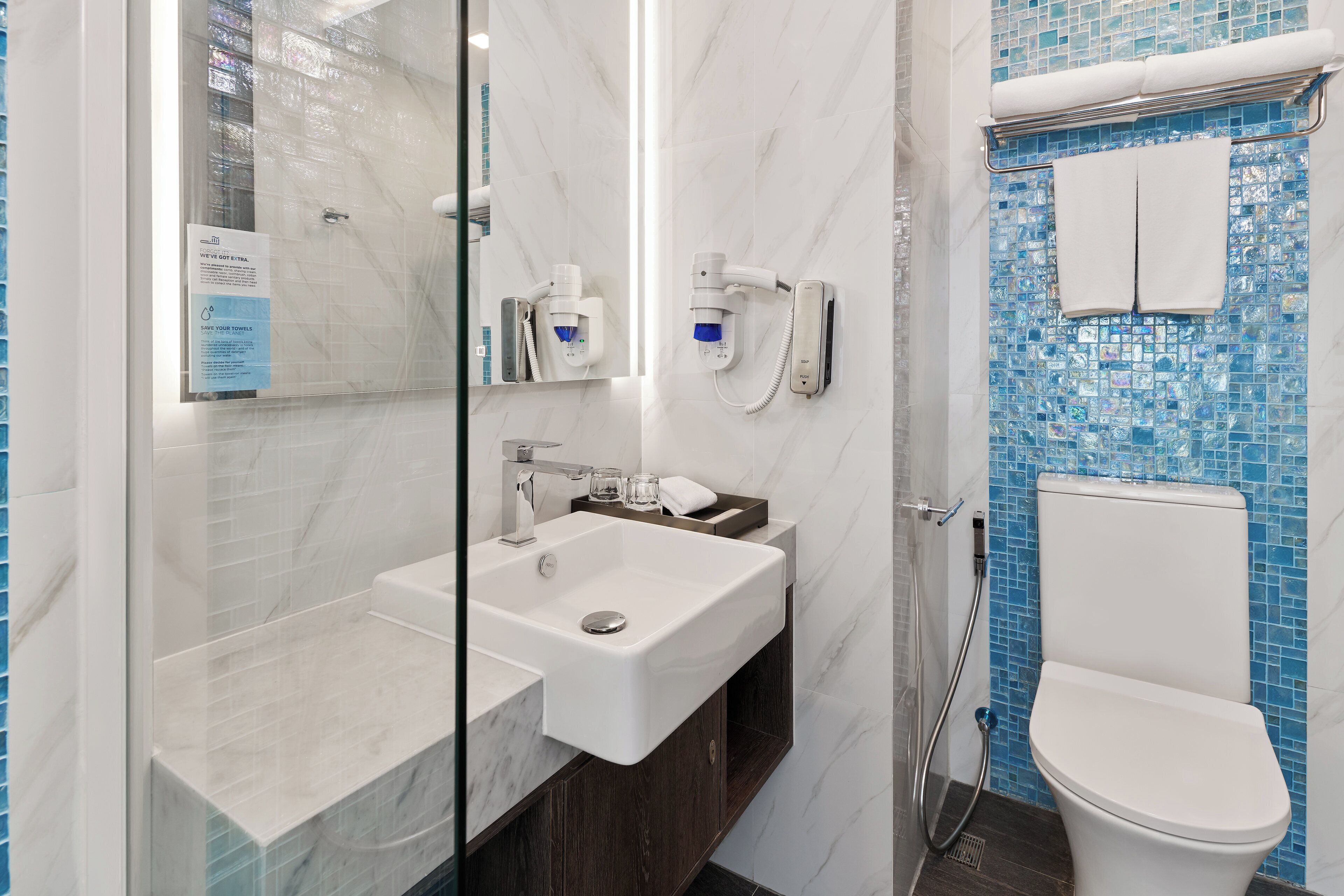 A bathroom with a glass-enclosed shower, a white sink, and a toilet with a blue mosaic tile wall.