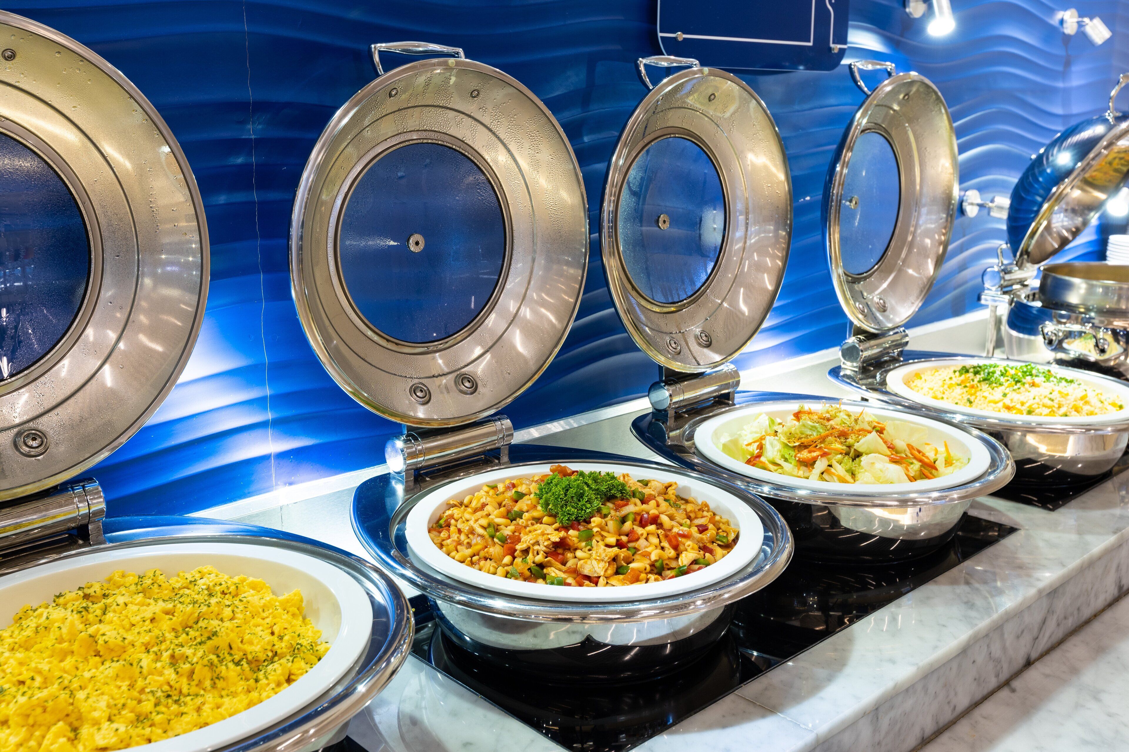 A buffet with various dishes in bowls and pots, set against a blue tiled wall.