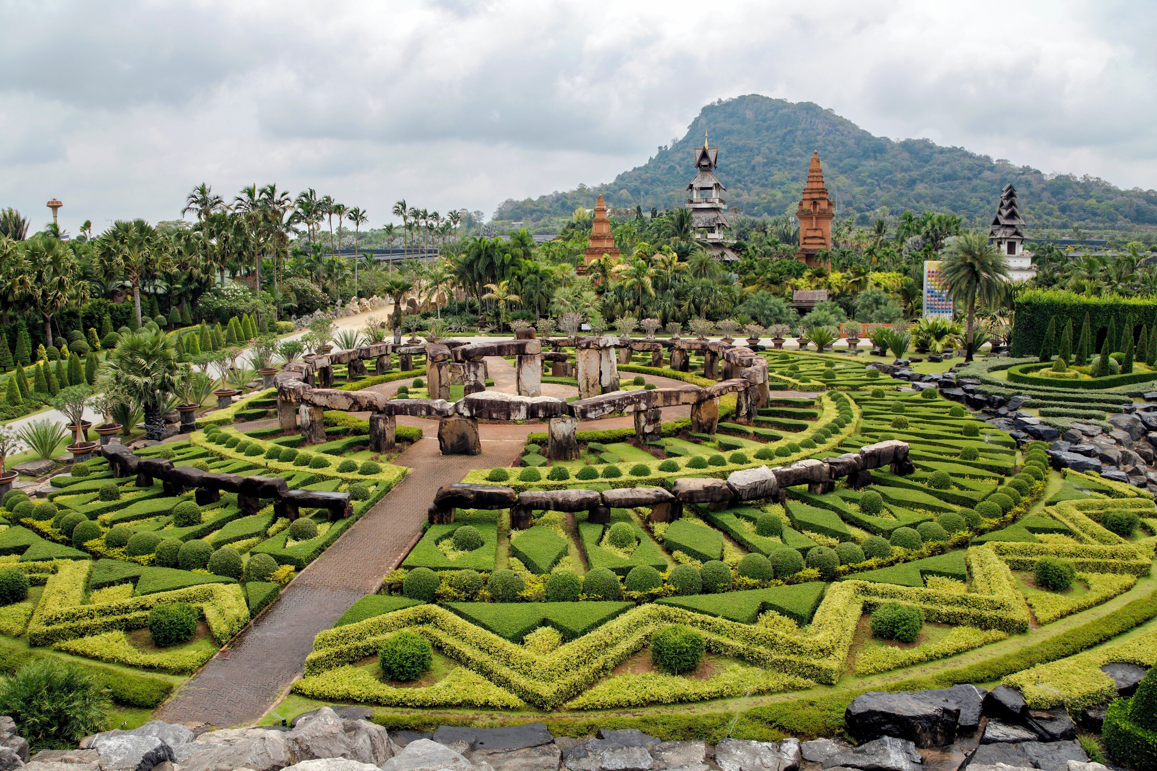 A well-manicured garden with geometric hedges, stone bridges, and traditional pagodas in the background.