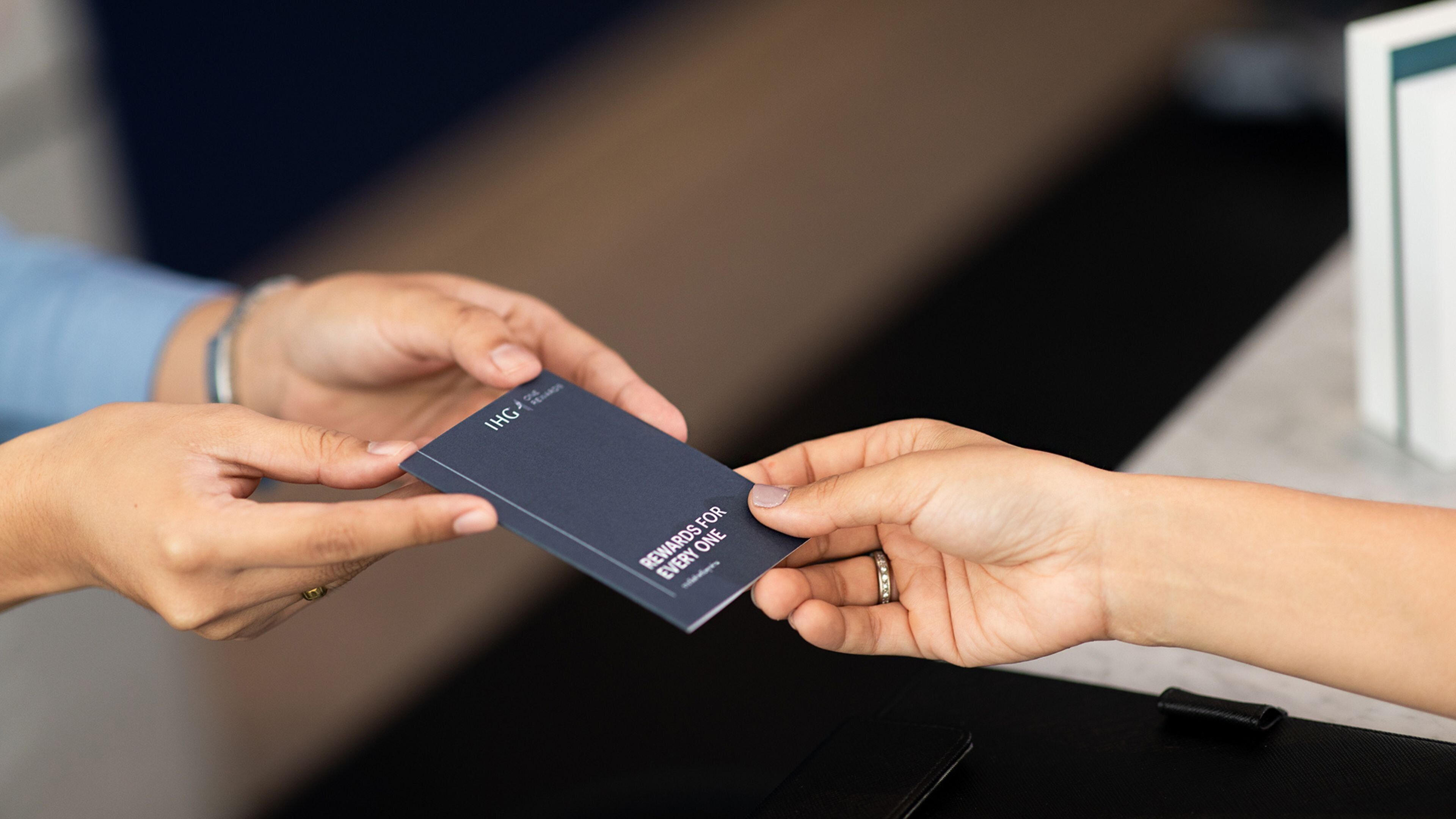 Une personne remet une carte de couleur sombre, sur laquelle figure un texte blanc, à une autre personne.