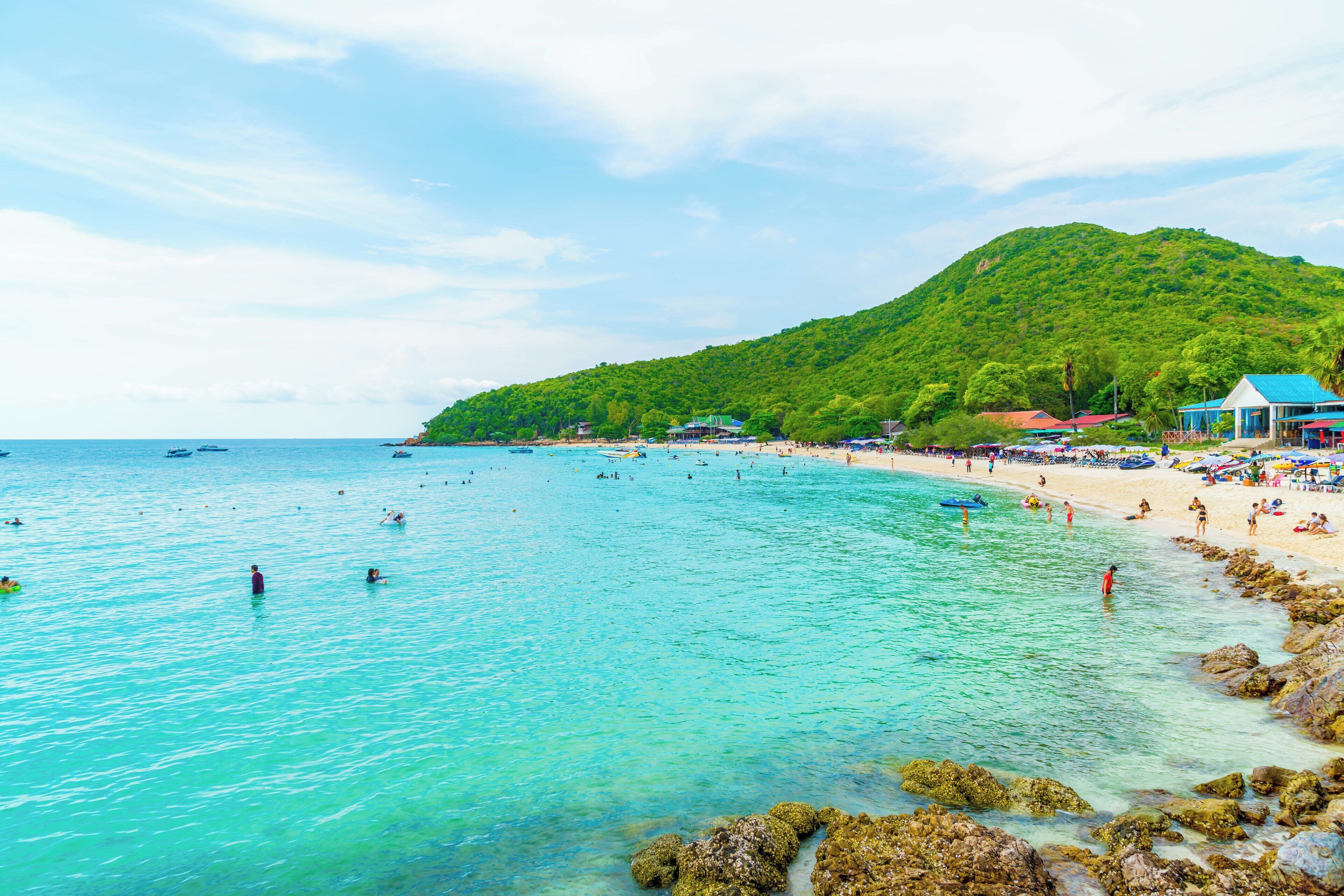 A beach with clear turquoise water, a sandy shore, and a lush green hill in the background.