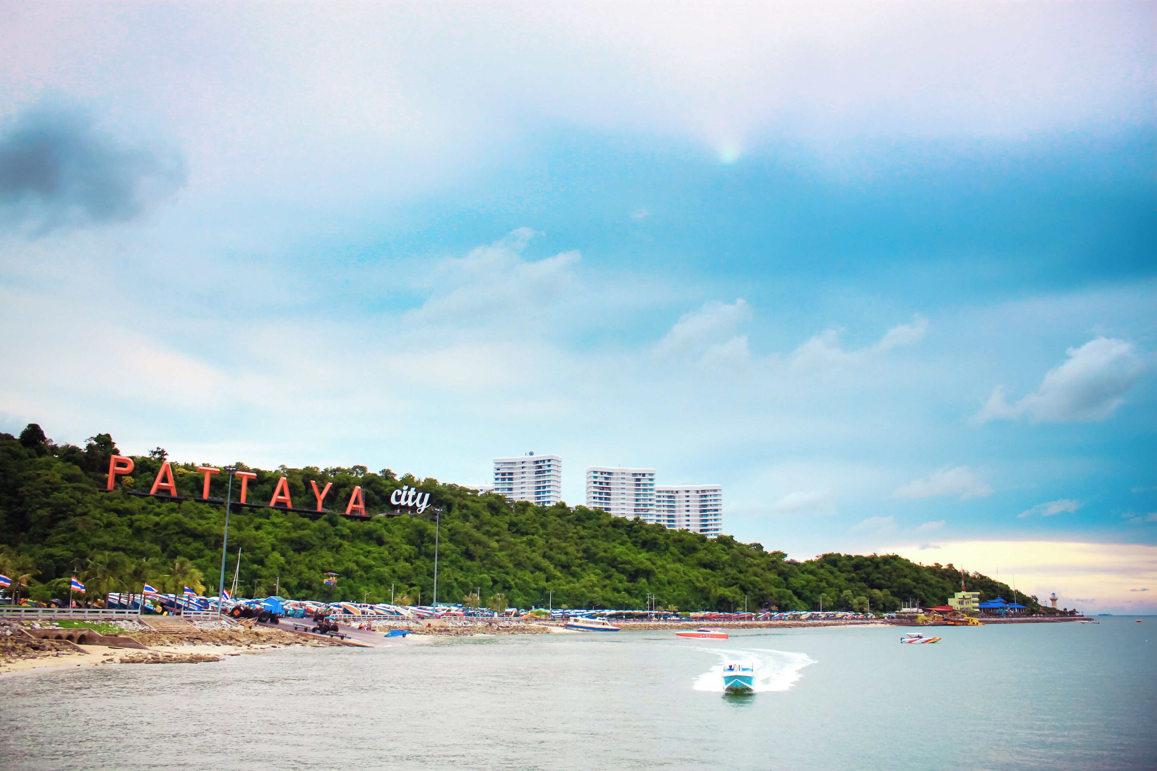 A beach with a sign reading 'Pattaya City' and a view of a water body with boats.