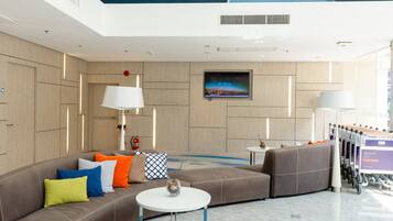 A modern hotel lobby with a large sofa, a round table, and a television on the wall.
