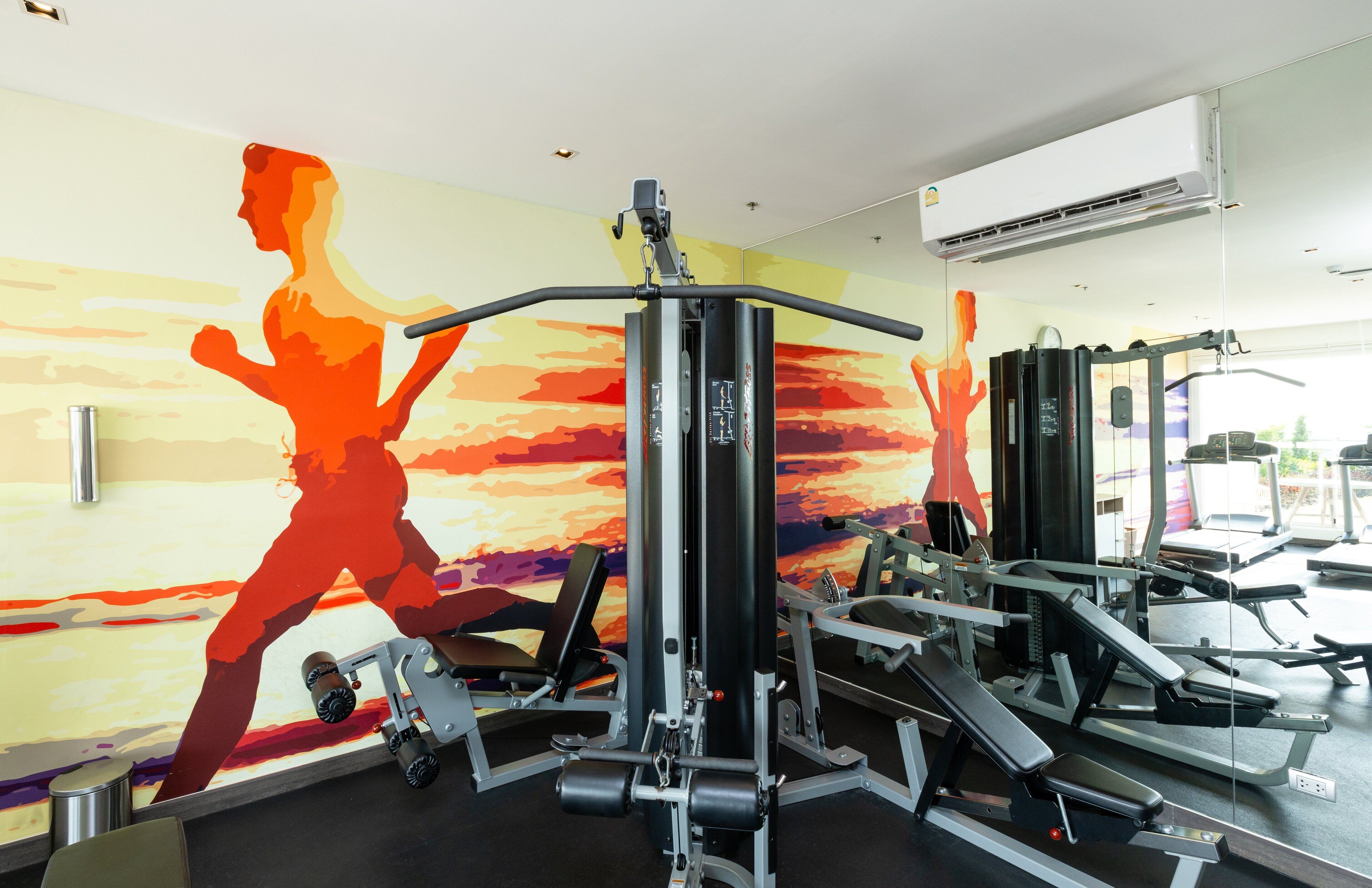A gym with exercise equipment and a mural of a running woman.