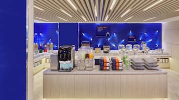 A modern hotel lobby with a coffee station, a digital kiosk, and a blue wall with text.