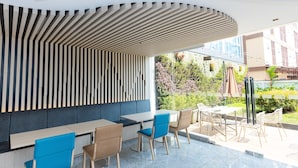Een moderne buitenruimte met een vloegvormige houten lamellenwand, tafels en stoelen.