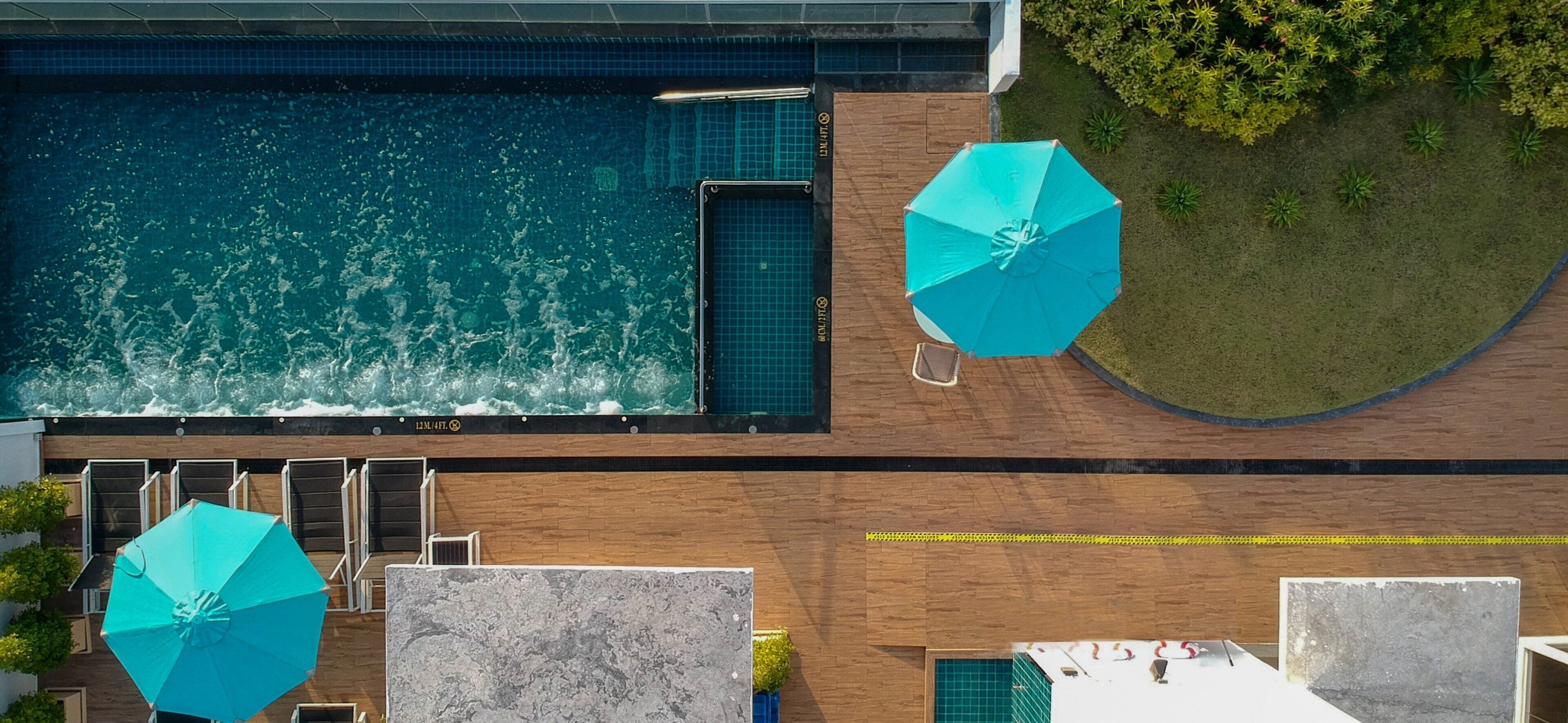 An aerial view of a swimming pool with two umbrellas and a wooden deck.