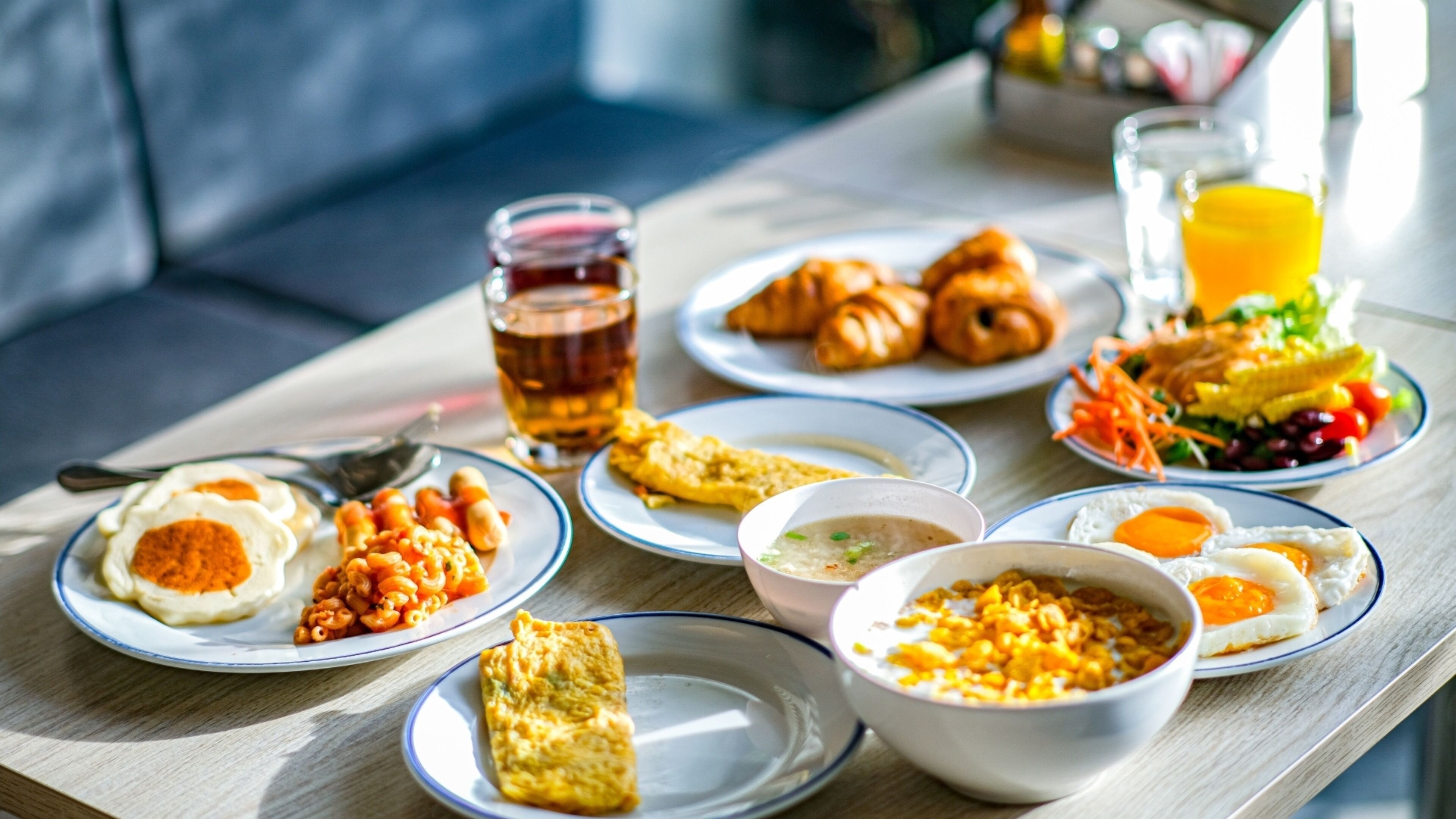A breakfast table with plates of eggs, croissants, and a salad.