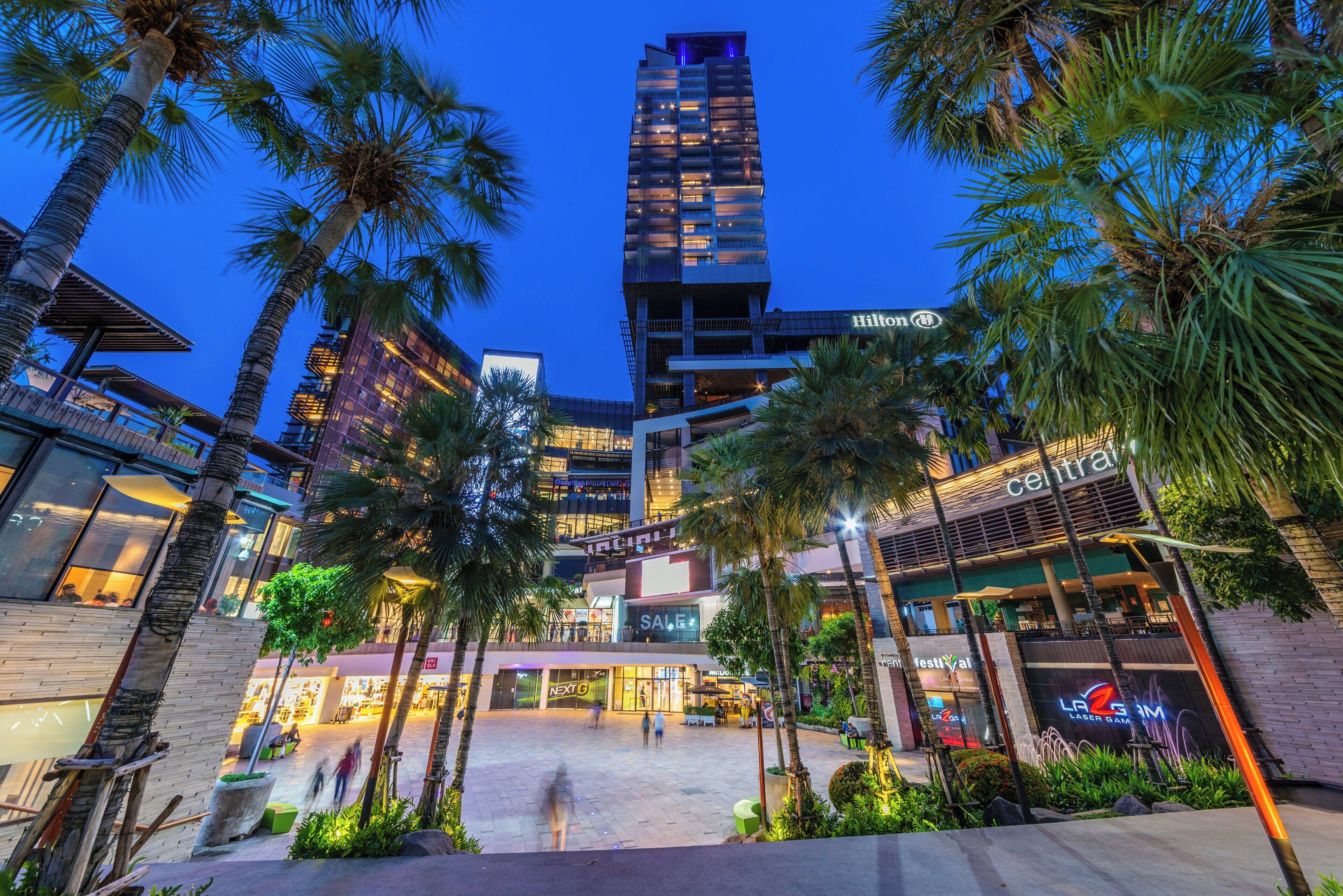 A modern hotel with a high-rise structure, a central plaza with palm trees, and various retail and dining establishments.