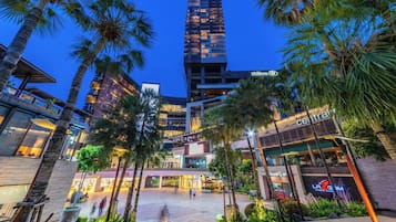 A modern hotel with a high-rise structure, a central plaza with palm trees, and various retail and dining establishments.