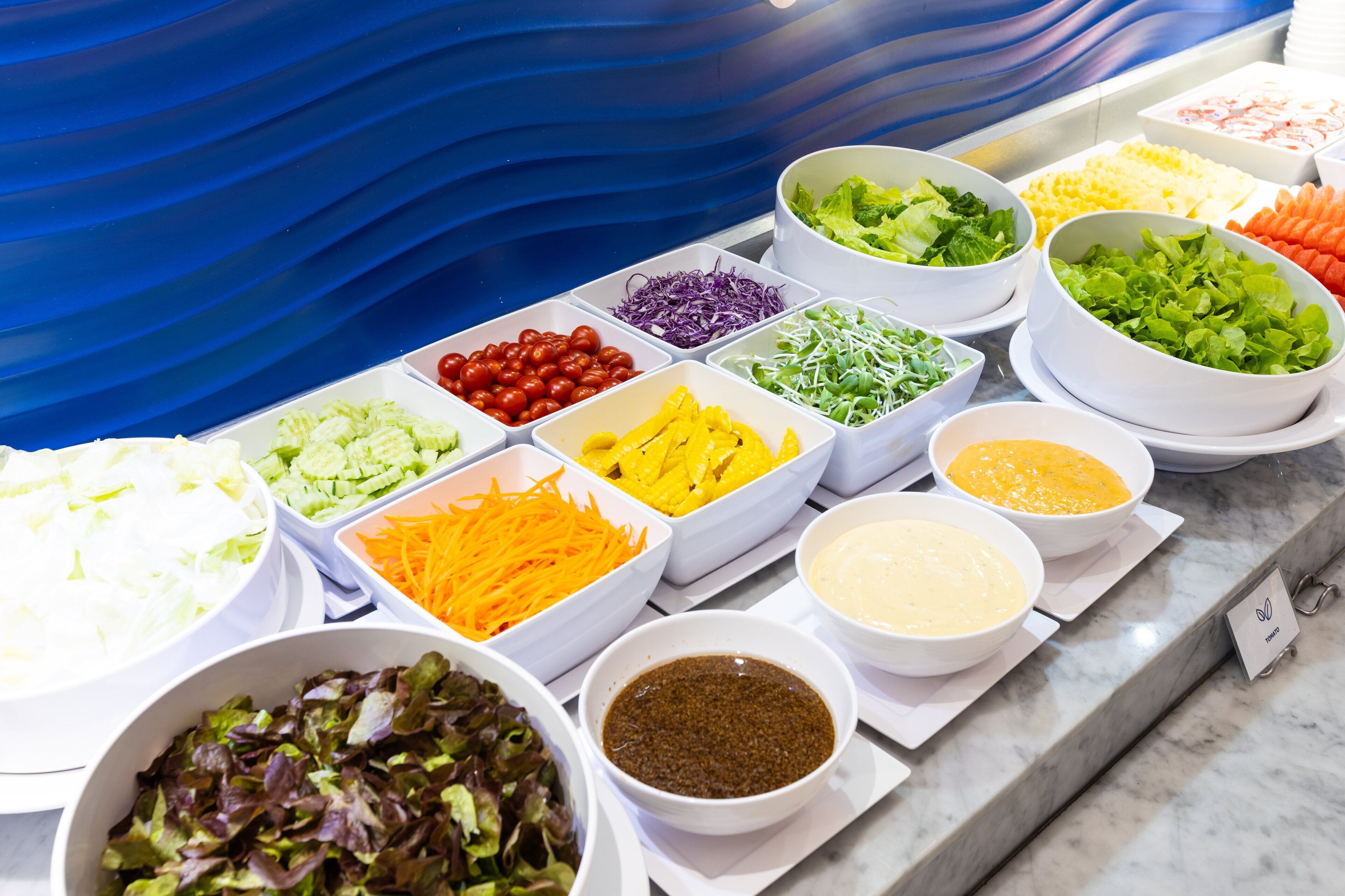 Un bufé con diversas opciones de comida, incluyendo ensaladas, verduras y salsas.