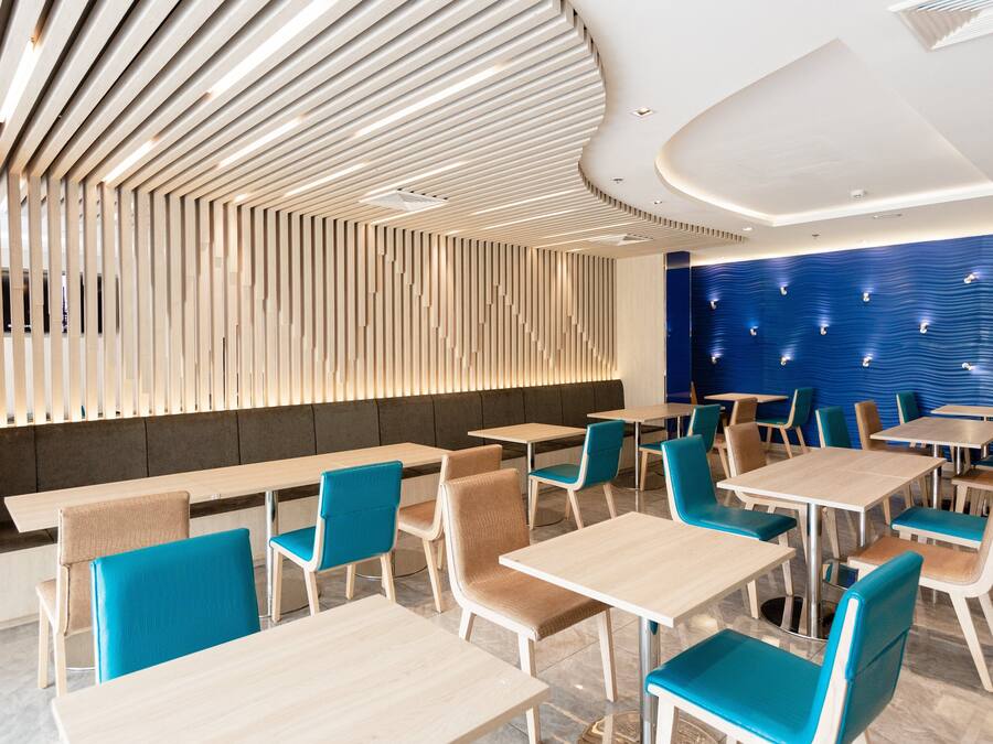 Un interior de restaurante moderno con techos de listones de madera, sillas tapizadas en azul y mesas de color claro.