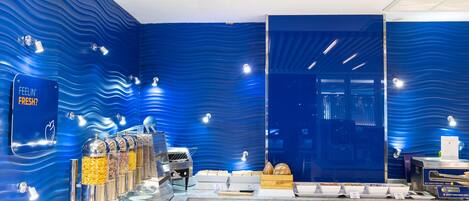 A breakfast buffet with self-serve stations, a large mirror, and a blue wavy wall design.