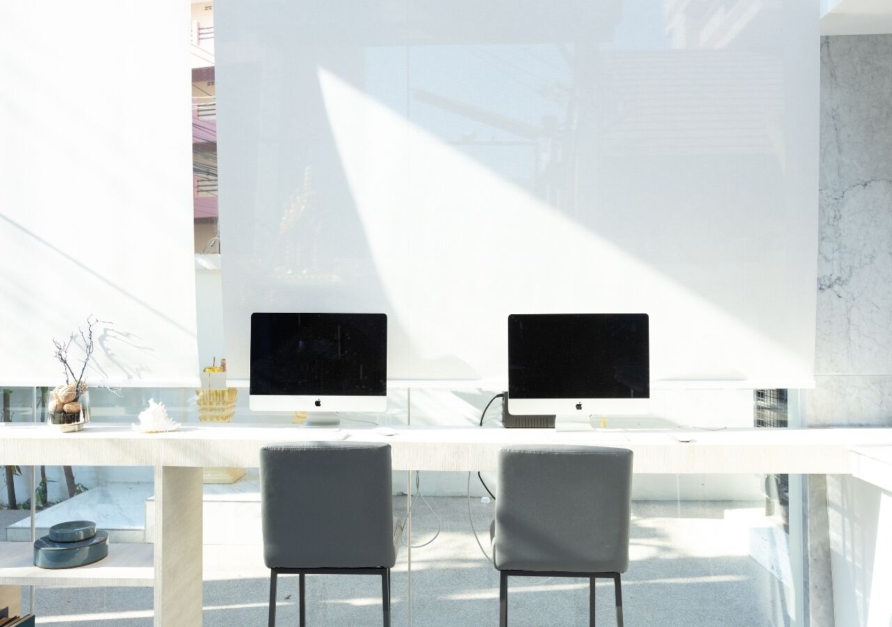 Un espace de bureau moderne avec deux ordinateurs Apple iMac sur un bureau blanc, deux chaises grises et une table en verre.