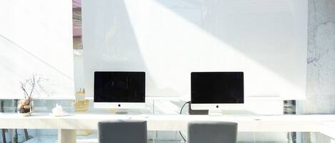 Un espace de bureau moderne avec deux ordinateurs Apple iMac sur un bureau blanc, deux chaises grises et une table en verre.