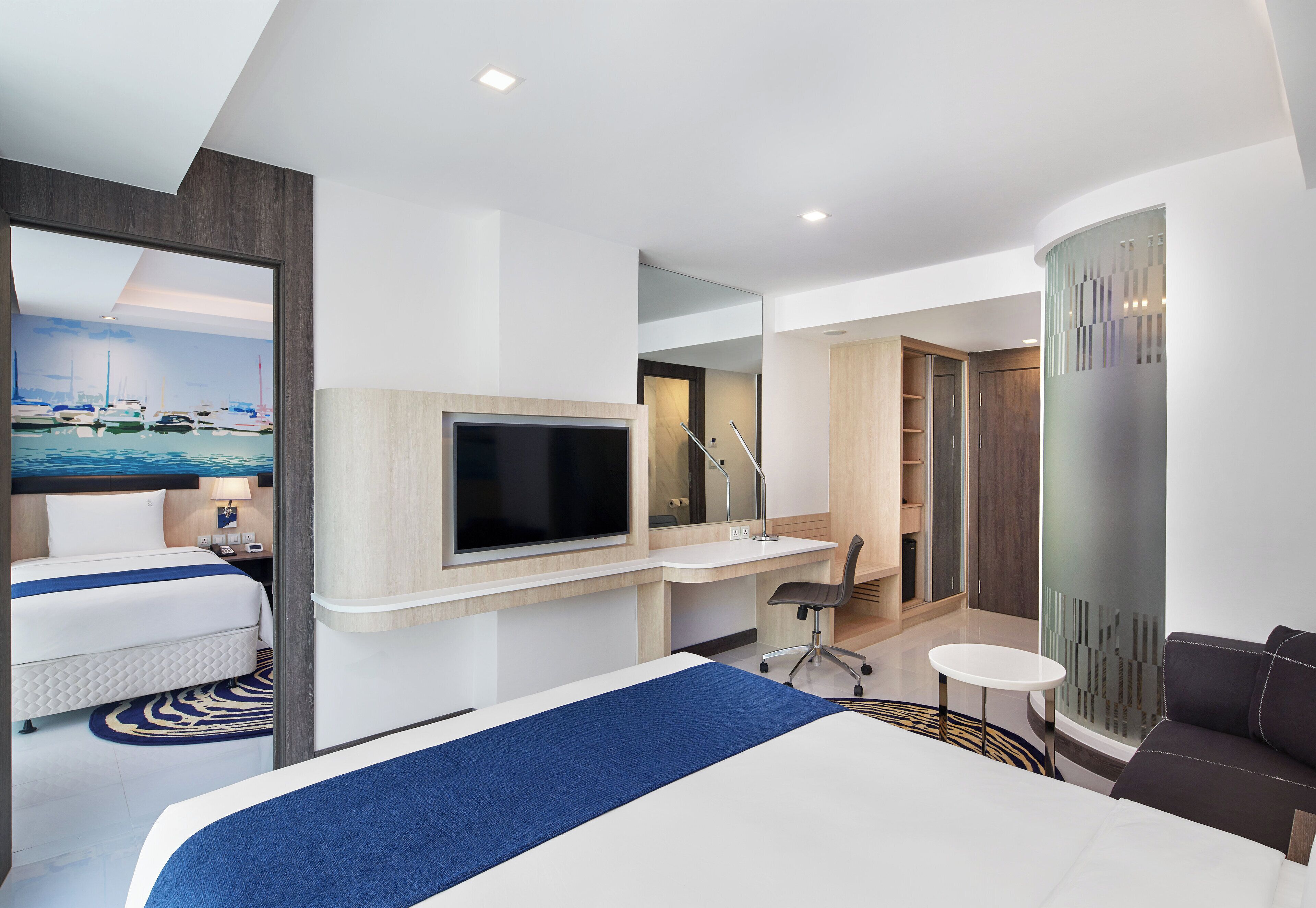 A hotel room with a bed, desk, TV, and a view of boats.