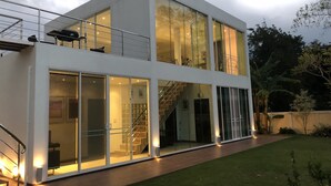 Un edificio moderno de dos plantas con grandes ventanales, una escalera a la vista y un césped bien cuidado.