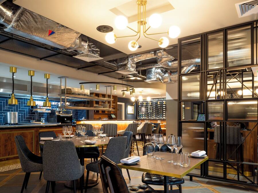 Ein modernes Restaurant-Interieur mit Barbereich, Esstischen und einer Weinauslage.
