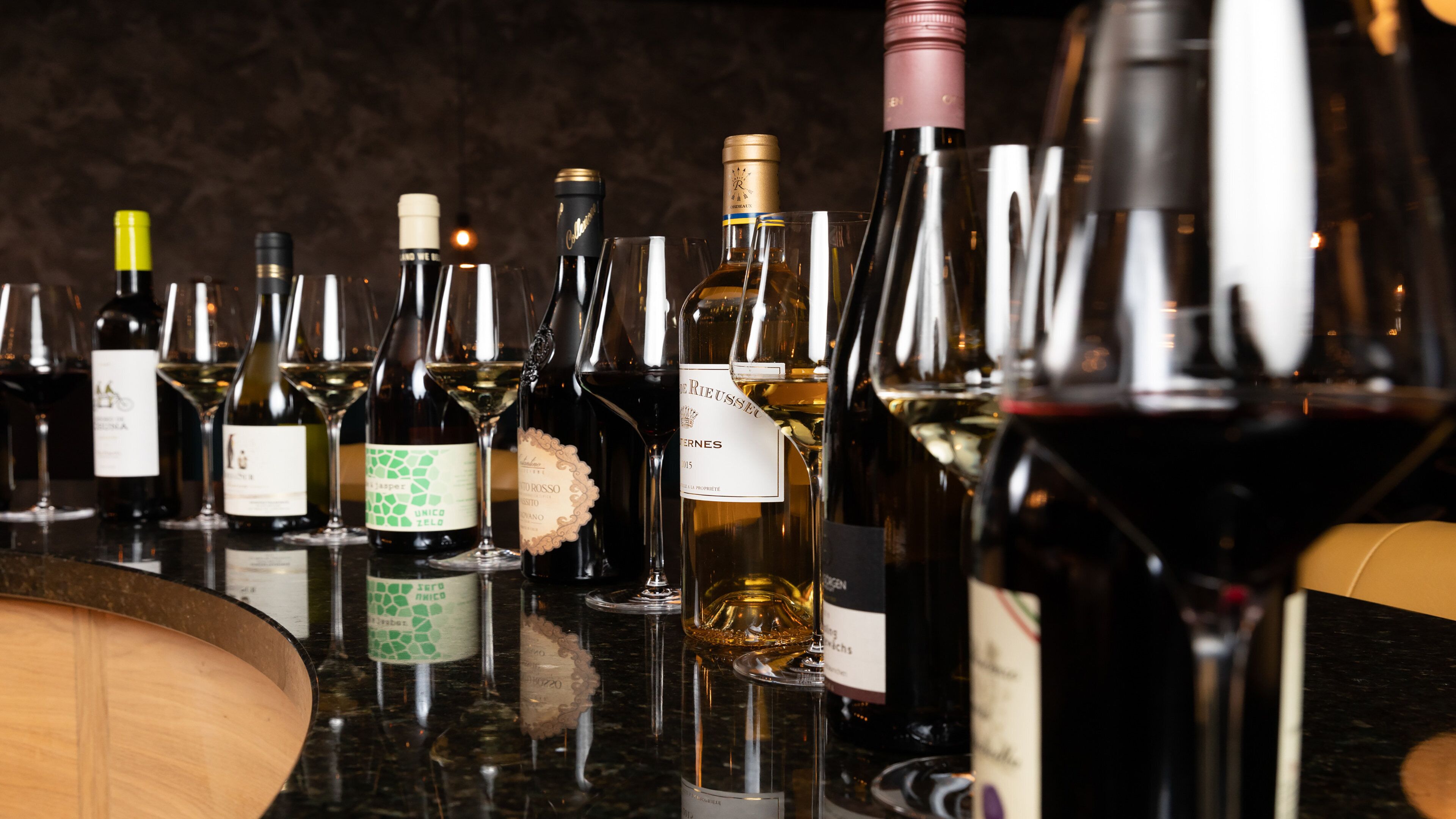 A variety of wine bottles and glasses on a bar counter.