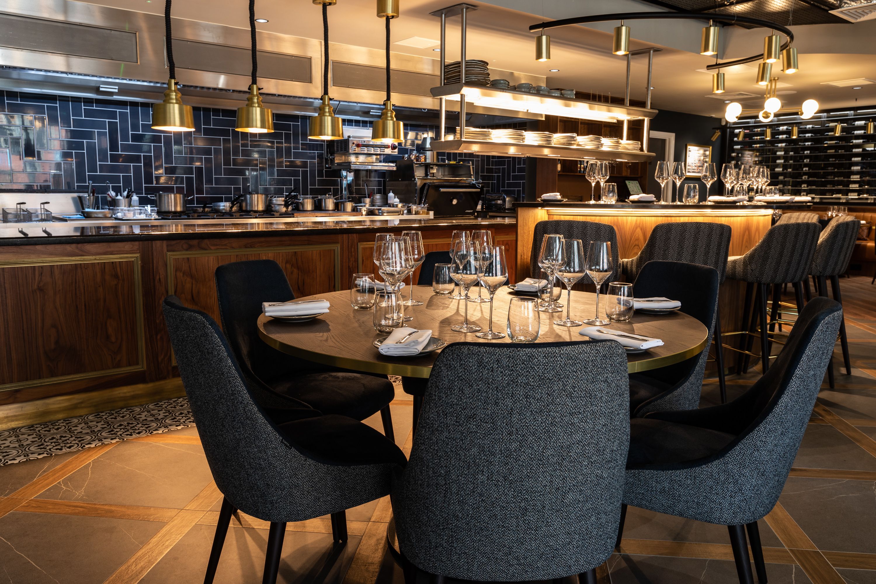 Un restaurant moderne avec une grande table à manger centrale, pouvant accueillir six personnes, entourée de chaises à l’assise rembourrée et au revêtement sombre.