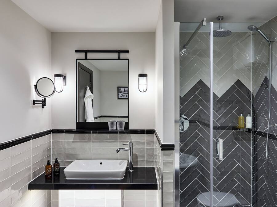 Une salle de bain moderne avec une douche carrelée en noir et blanc, un grand miroir et un lavabo doté d’un plan de travail noir.