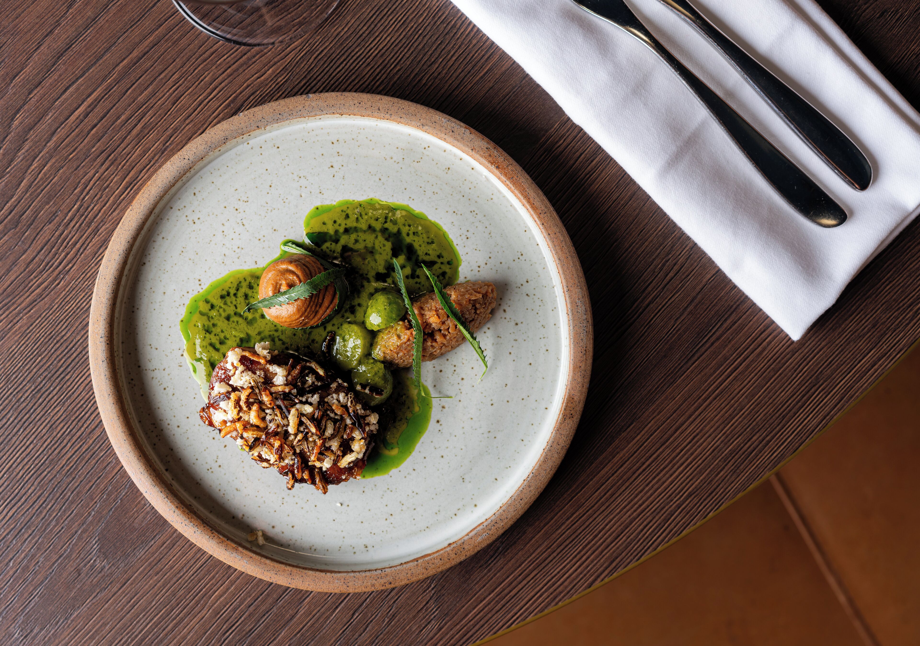 A plate of food on a wooden table with a white napkin and silverware.