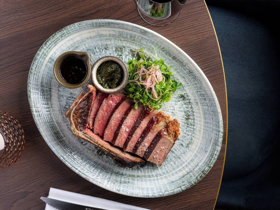 A plate with sliced meat, greens, and two sauces on a ceramic plate.