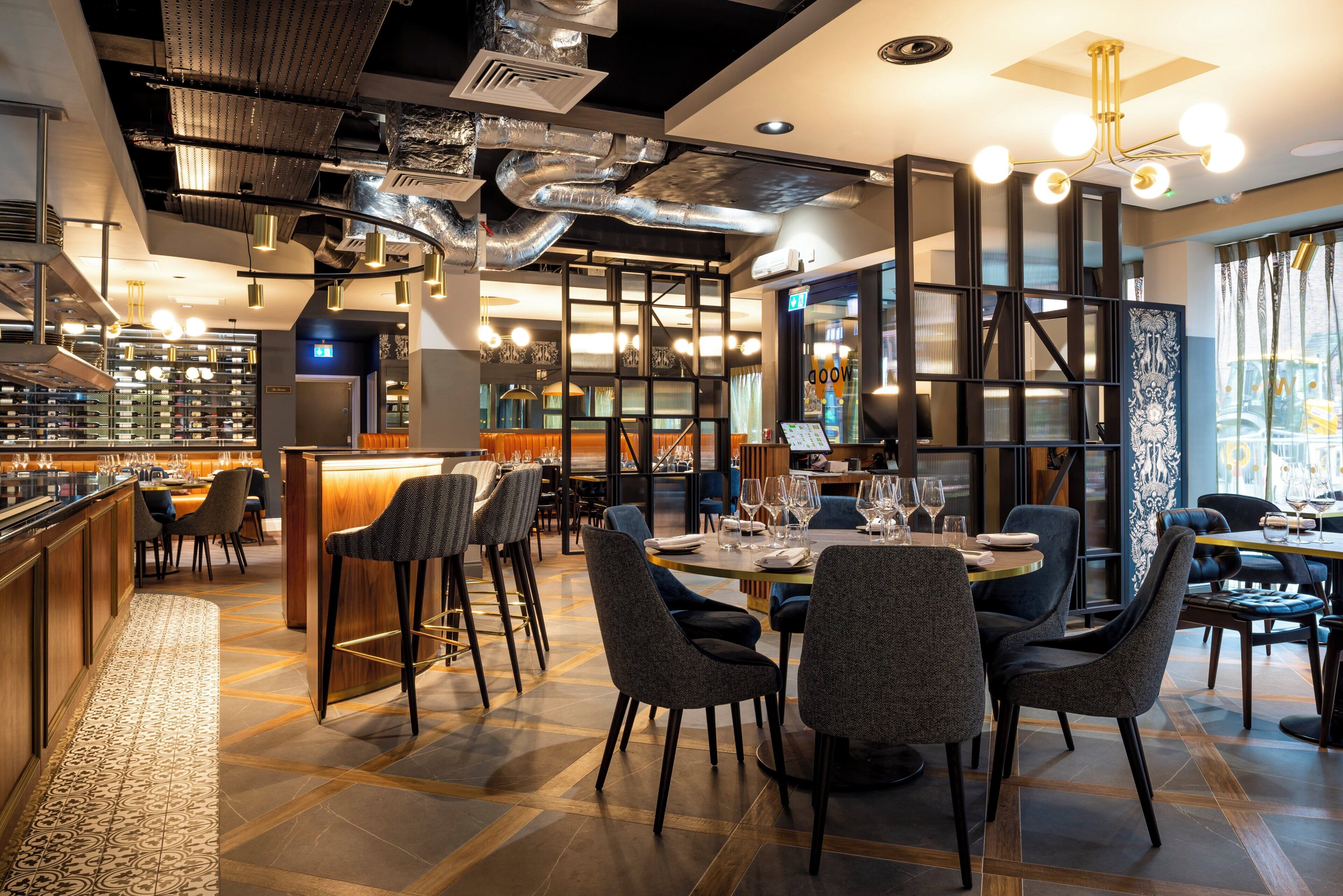 Un interior de restaurante moderno con zona de bar, techo alto con conductos expuestos y luminarias contemporáneas.