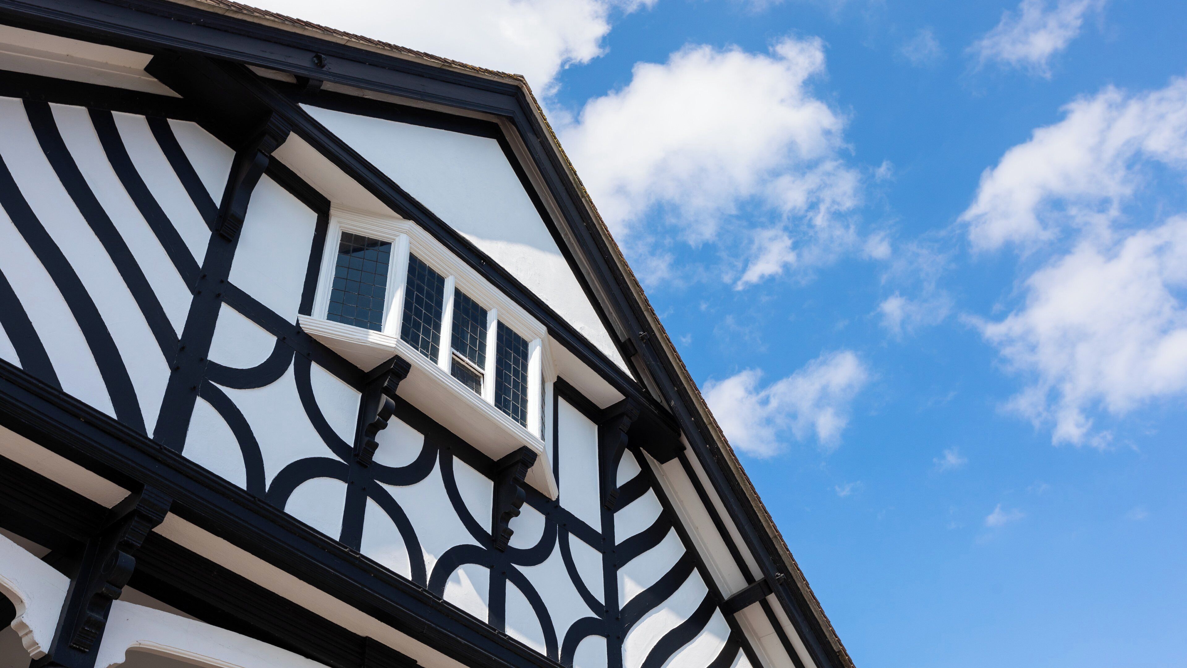 A building with a distinctive black and white facade, a visible window, and a clear blue sky with clouds.