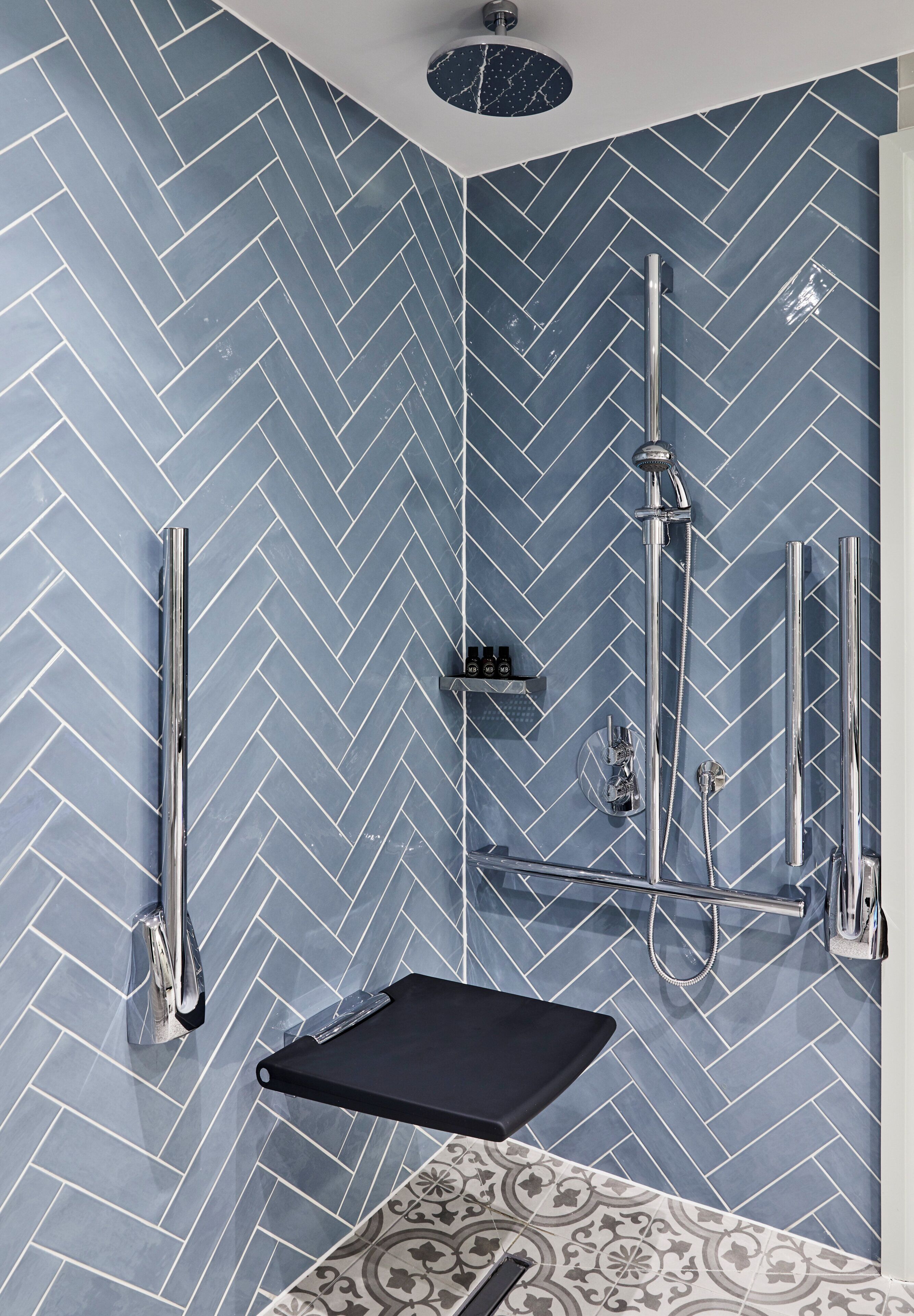 Une salle de bain moderne avec un carrelage disposé en motif chevron, une douche à l’italienne et un meuble-lavabo noir.
