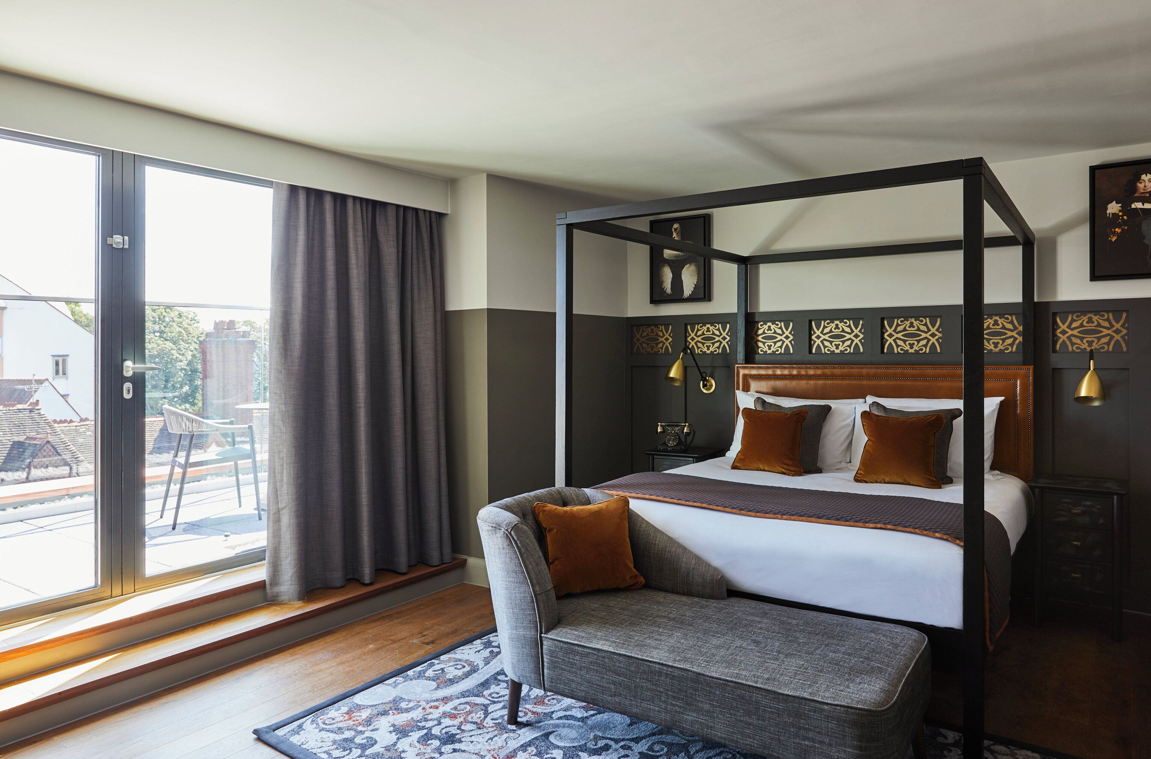 A four-poster bed with a dark headboard, a grey armchair, and a patterned rug.