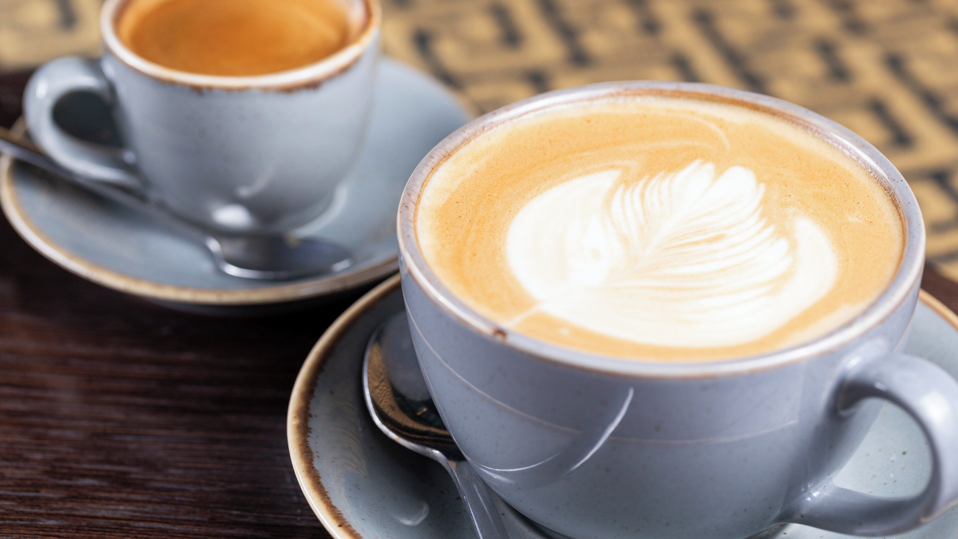 Dos tazas de café con diseños de latte sobre una mesa de madera.