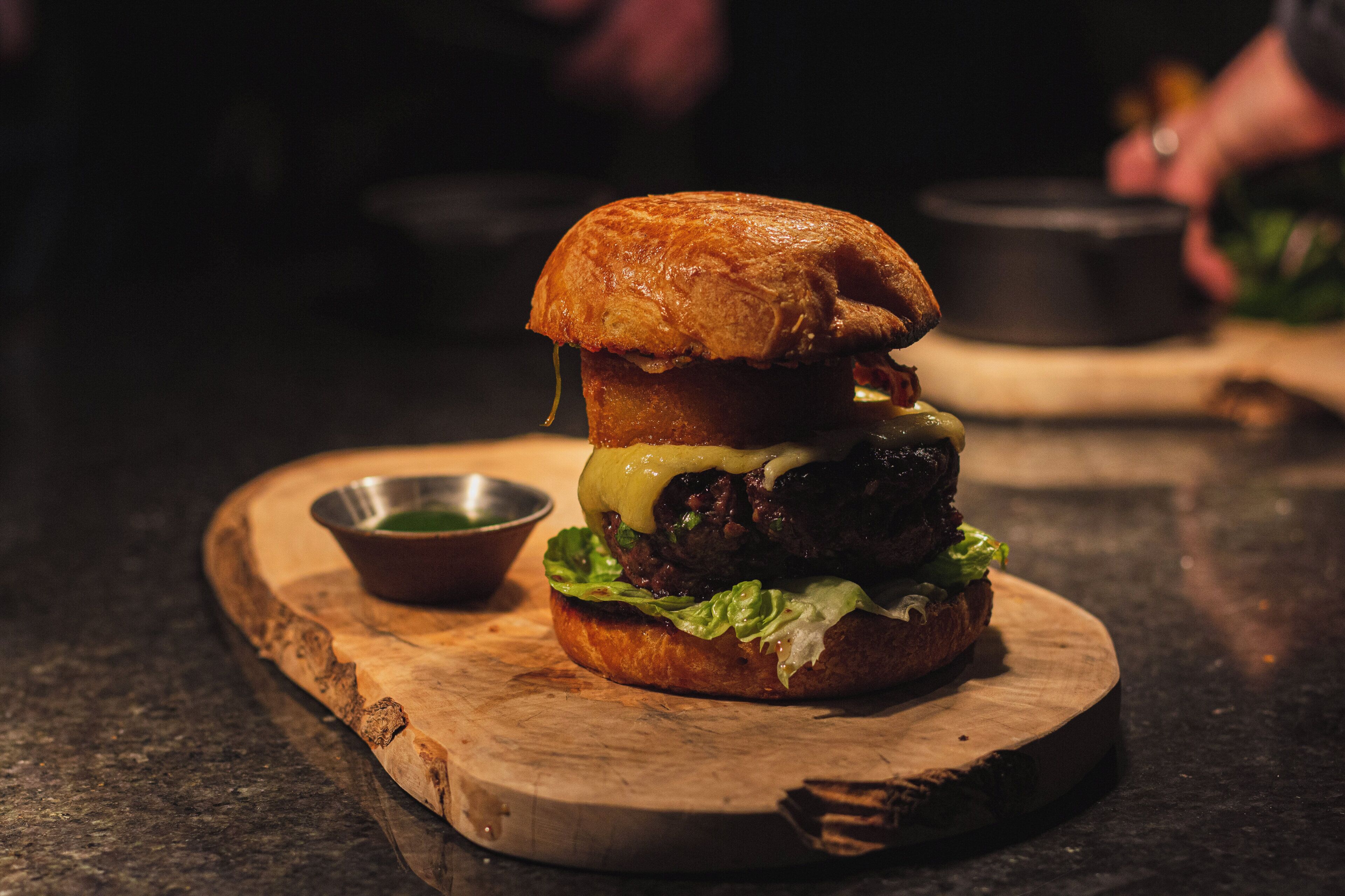 A burger on a wooden board with a small bowl of sauce.