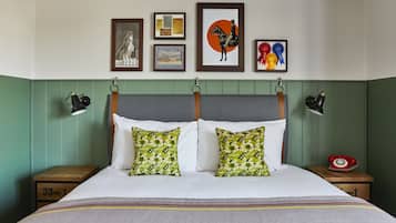 A neatly arranged bedroom with a bed, two nightstands, a red rotary phone, and framed artwork on the wall.