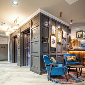 A hotel lobby with a grand staircase, a bar area, and a seating area with blue upholstered chairs.