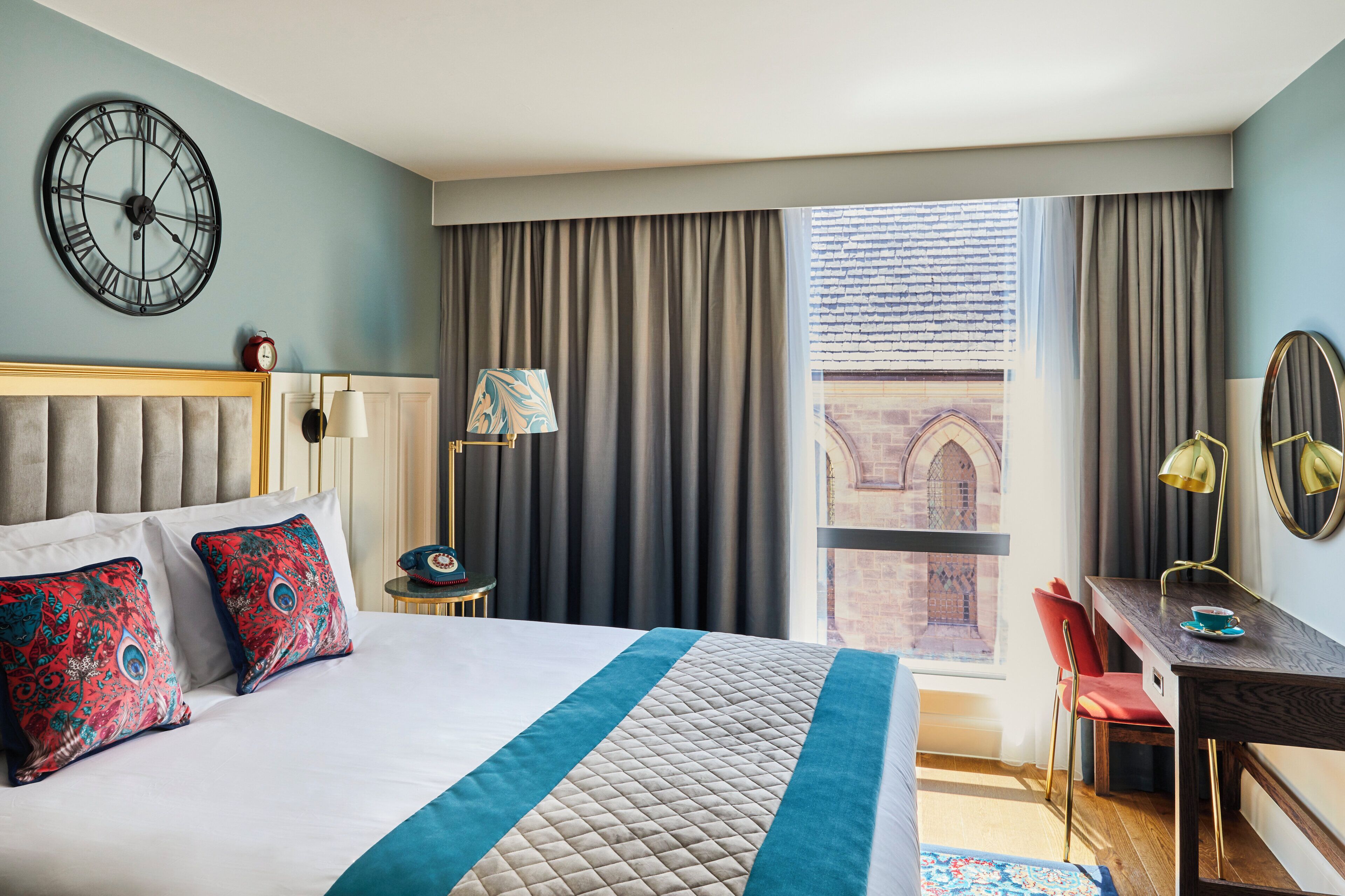 Ein Hotelzimmer mit Bett, Schreibtisch, Stuhl, einer Uhr und Blick nach draußen.