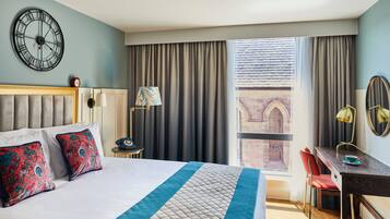 Ein Hotelzimmer mit Bett, Schreibtisch, Stuhl, einer Uhr und Blick nach draußen.