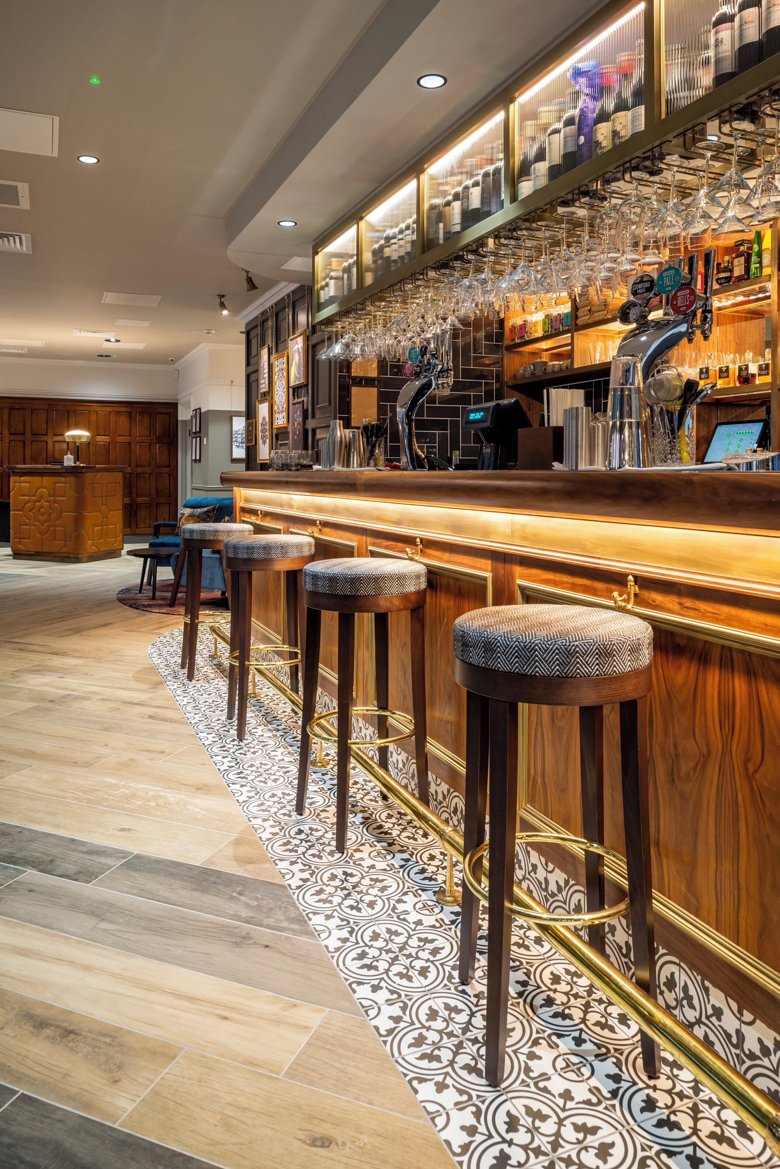 A bar area with a wooden counter, multiple stools, and a variety of glassware and bottles.